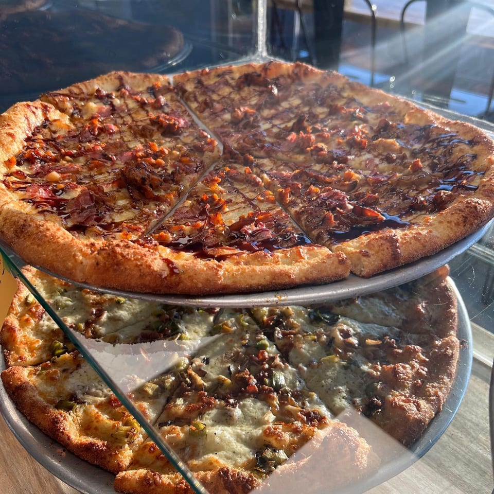 Two PEEL pizzas, one with BBQ chicken and the other with white sauce and artichokes, stacked on display.