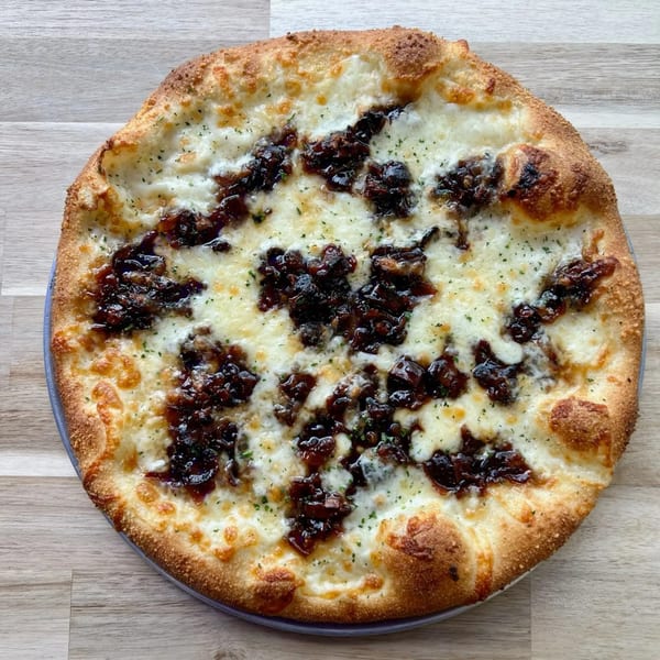 PEEL pizza with white cheese, caramelized onions, and herbs on a light wooden table.