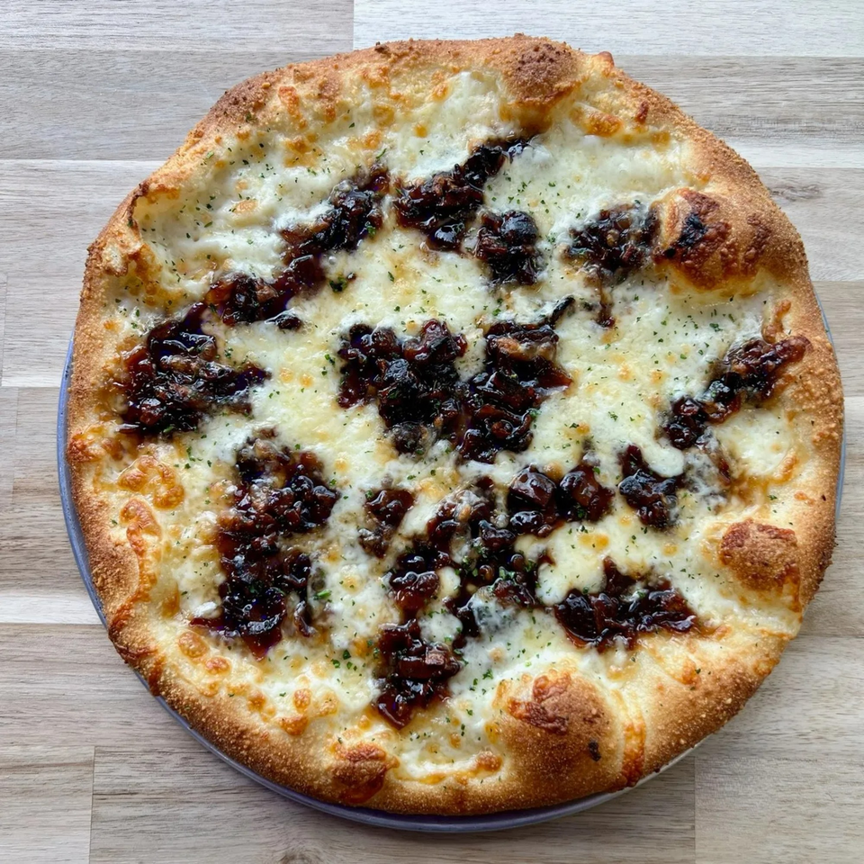 PEEL pizza with white cheese, caramelized onions, and herbs on a light wooden table.