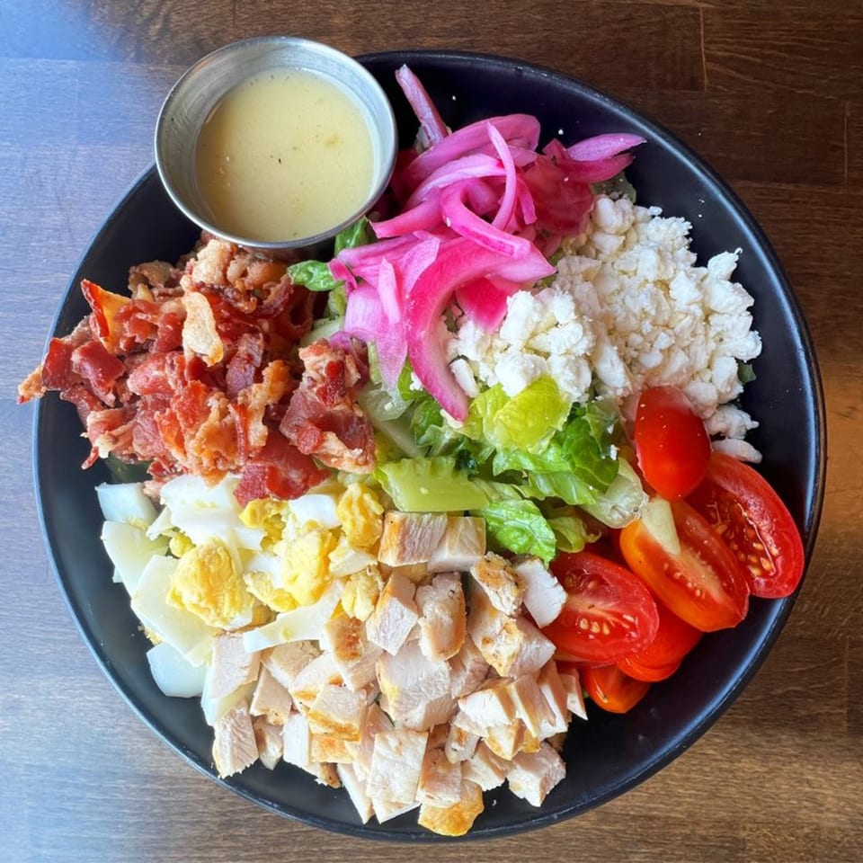 A vibrant salad with chicken, bacon, tomatoes, eggs, pickled onions, and feta cheese.
