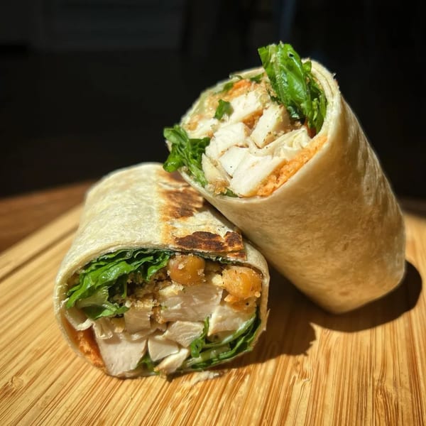Two chicken wraps, filled with lettuce and chickpeas, on a wooden cutting board.