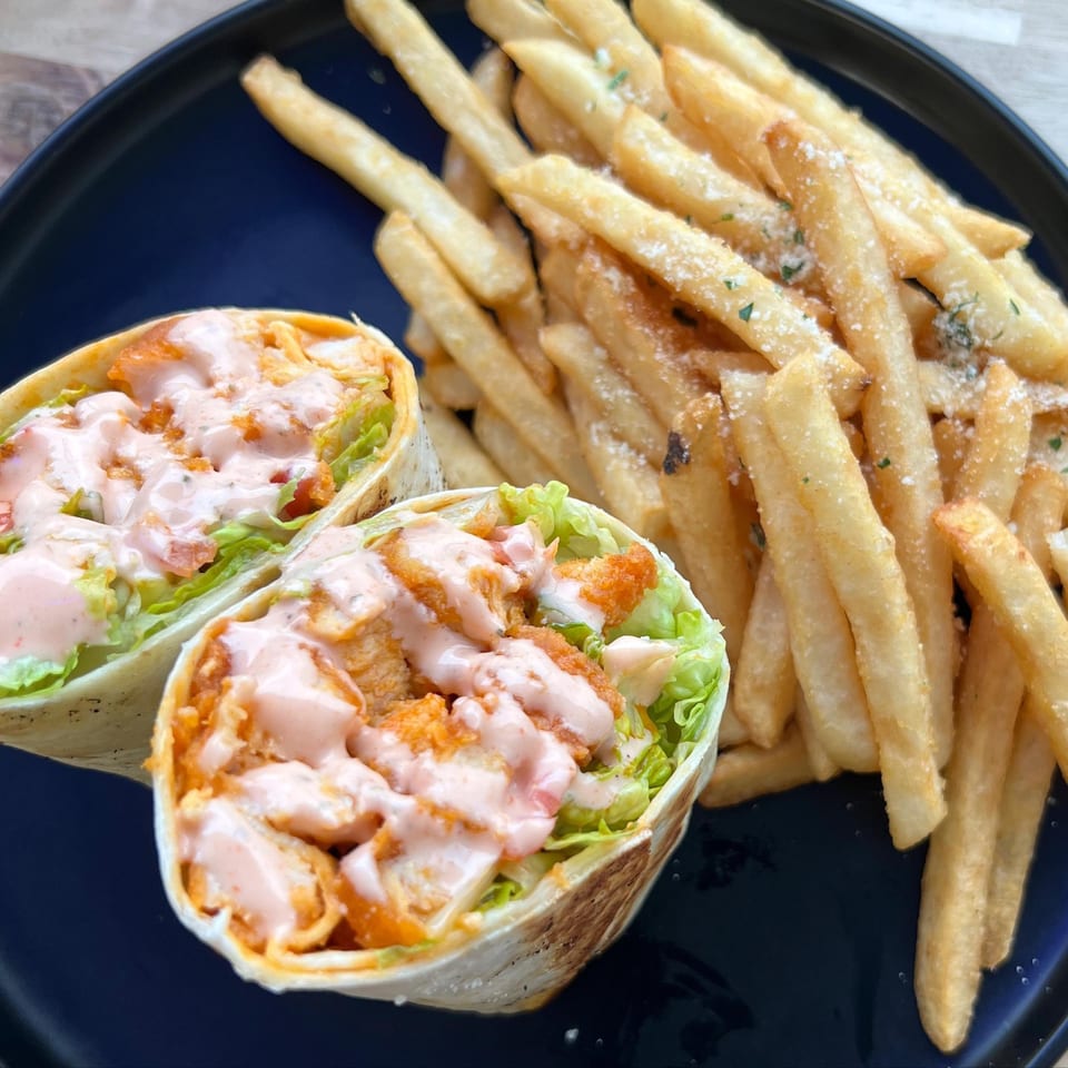 Two buffalo chicken wraps with lettuce and pink sauce, served with a side of french fries.