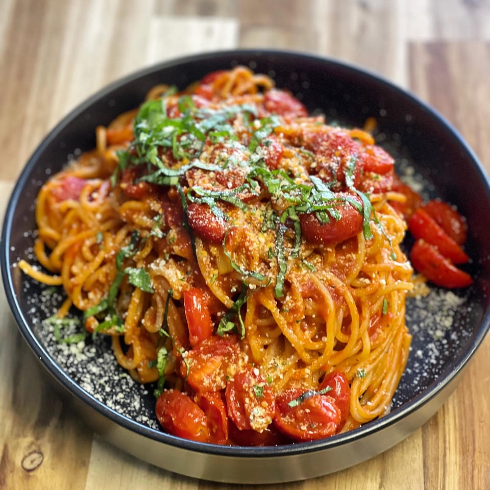 Spaghetti with cherry tomatoes, basil, and parmesan cheese in a black bowl on a wooden table.