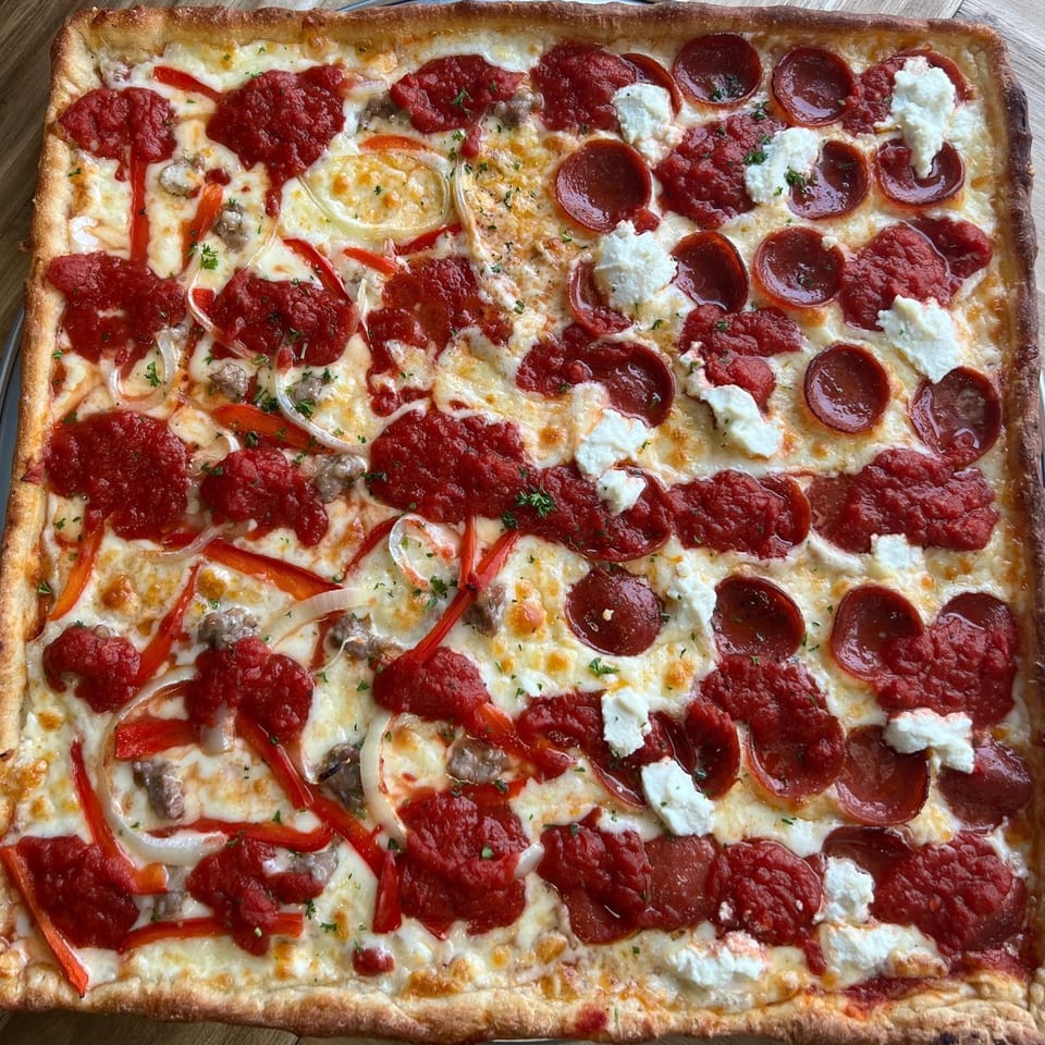 A square PEEL pizza with half pepperoni and ricotta, half sausage, peppers, and onions.