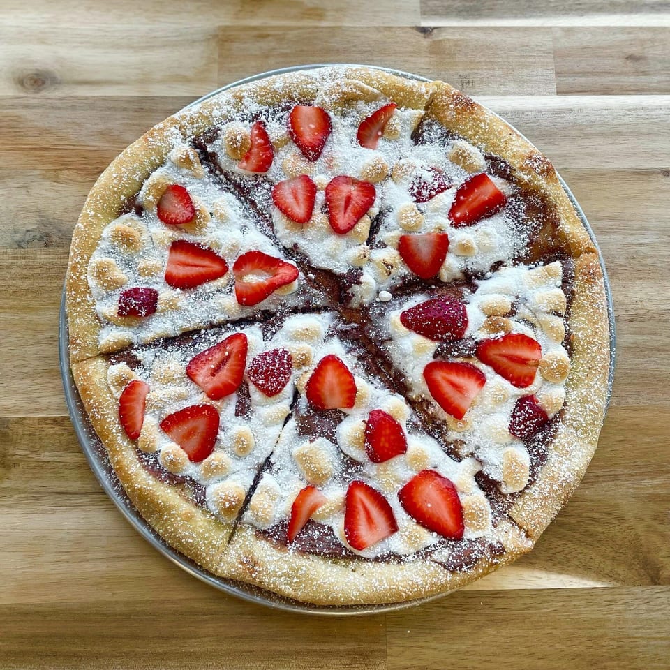 PEEL's dessert pizza with chocolate, marshmallows, strawberries, and powdered sugar on a wooden table.