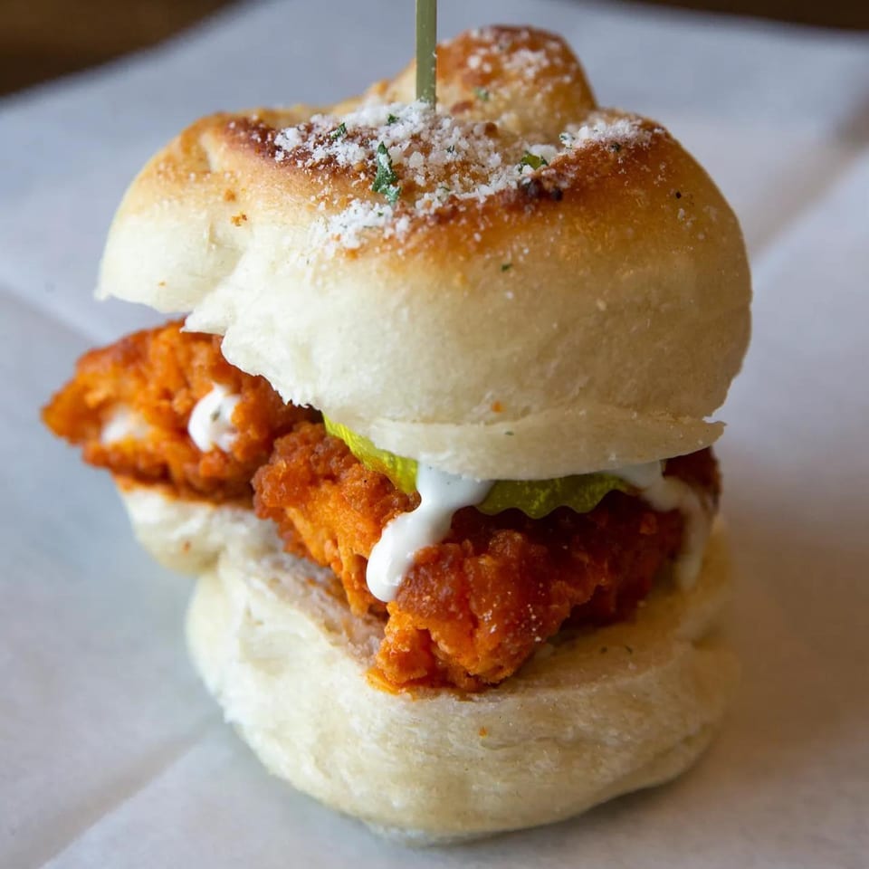 A PEEL chicken slider with crispy chicken, pickles, and white sauce on a bun.