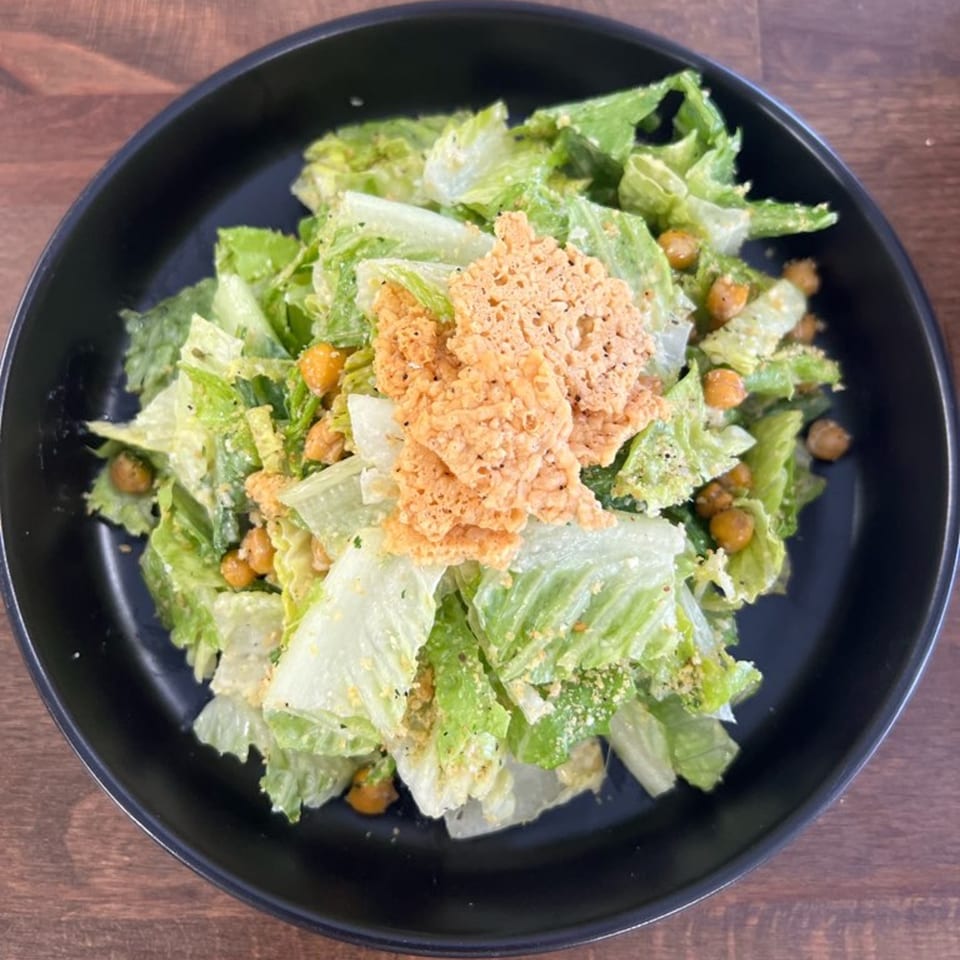 PEEL's Caesar salad with romaine lettuce, chickpeas, and crispy cheese crisps in a black bowl.